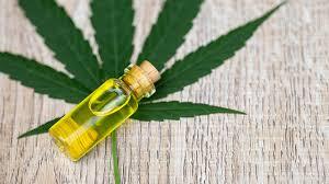 CBD oil bottle with cork stopper beside a large green cannabis leaf on a rustic wooden surface