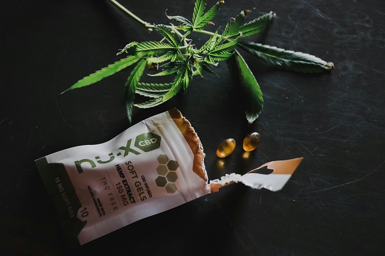 Nu-x CBD hemp extract soft gels packet with softgel capsules and cannabis leaves on dark background
